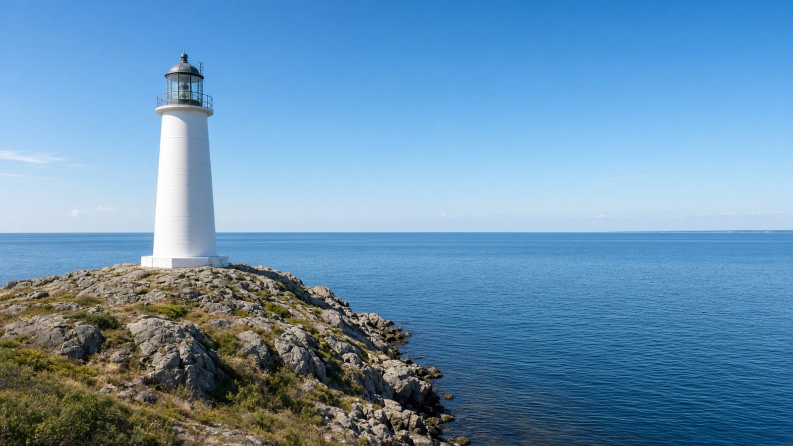White lighthouse on a rocky point above a calm blue sea